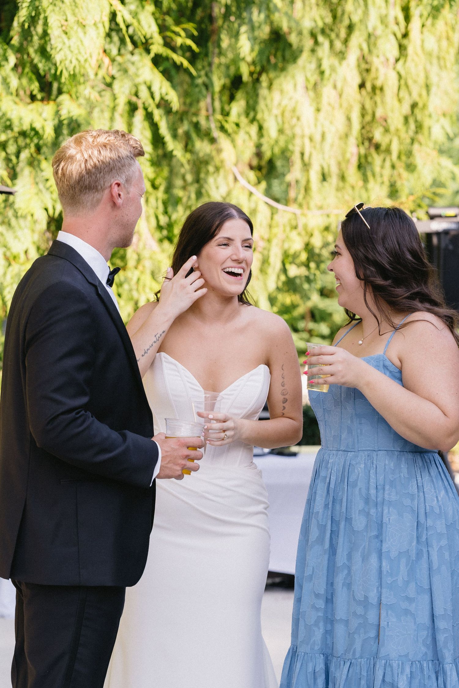 Bride laughing joyfully with wedding guests while holding champagne at outdoor reception.