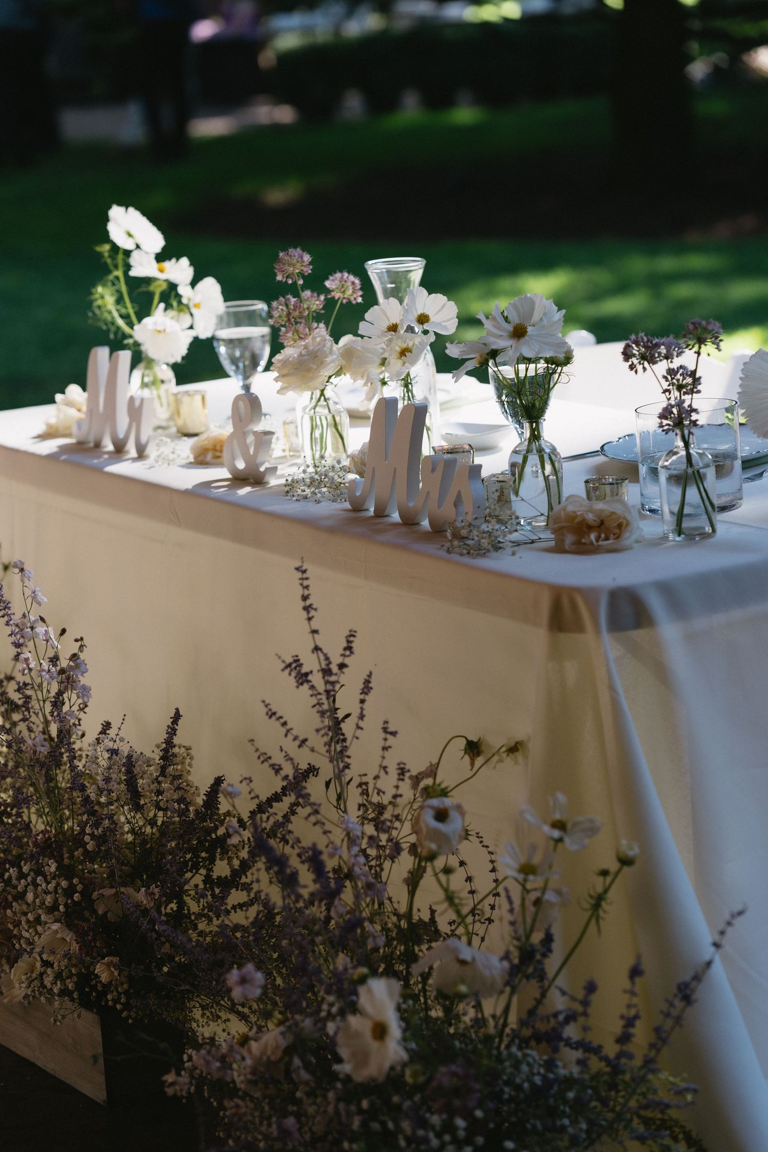 Elegant outdoor wedding table with white floral arrangements, lavender, and delicate place settings.