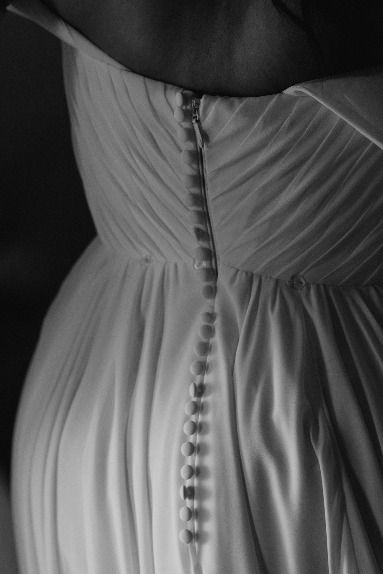 Black and white close-up of a wedding dress back featuring delicate button details and a zipper closure.