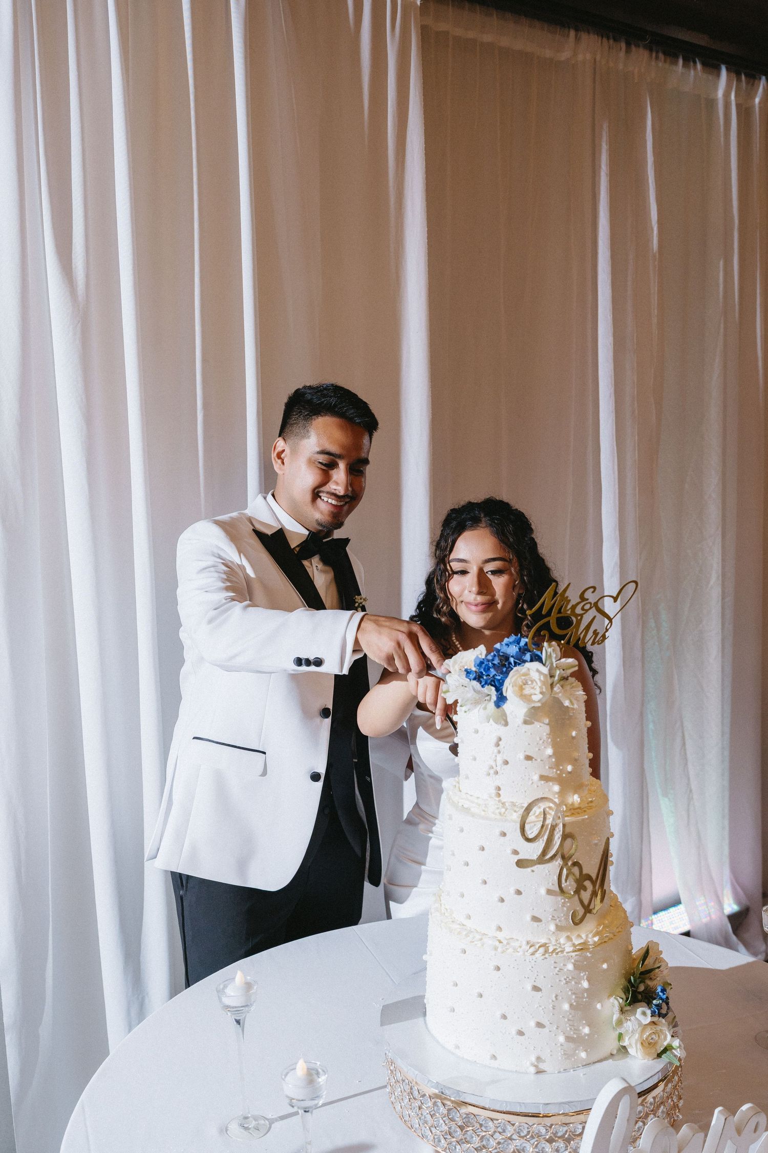 Smiling bride and groom cutting their elegant white wedding cake together.
