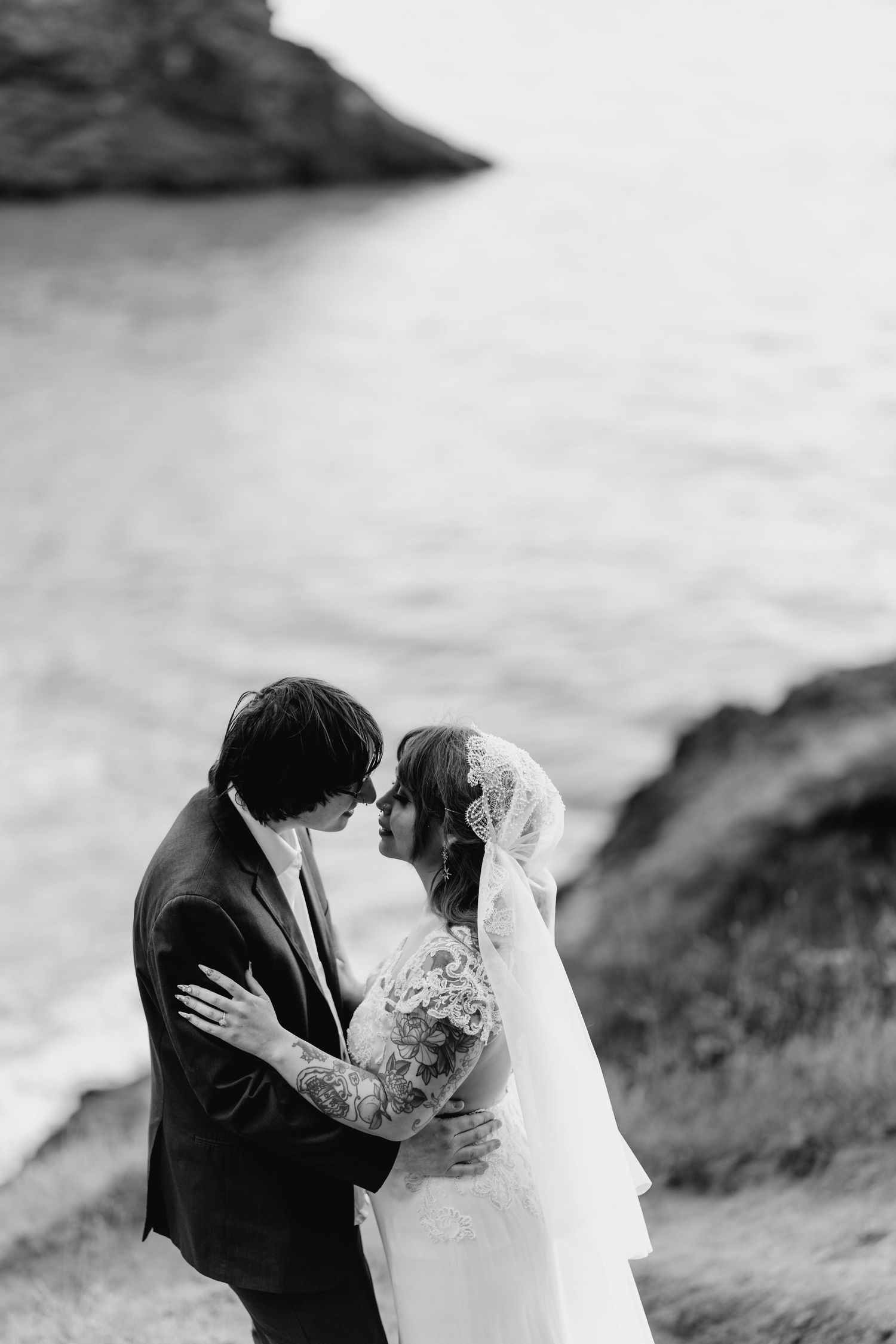 Bride and groom share an intimate moment embracing near the ocean in black and white photo.