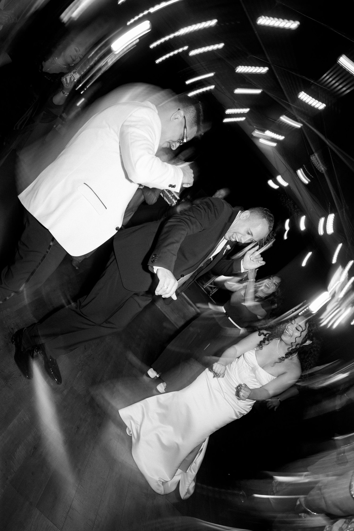 Dynamic black and white wedding reception dance floor photo with motion blur and swirling light trails.