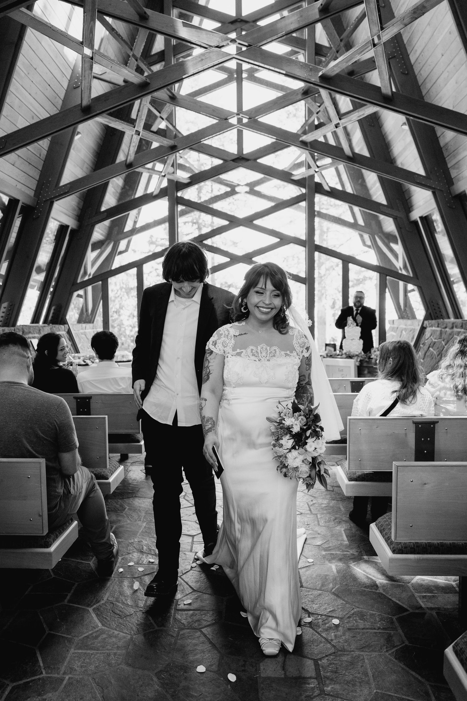 Black and white photo of bride and groom walking down the aisle of a beautiful wooden chapel.