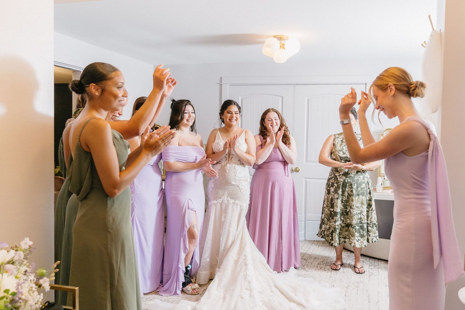 Bridesmaids in purple and green dresses cheering for bride in white lace wedding gown.