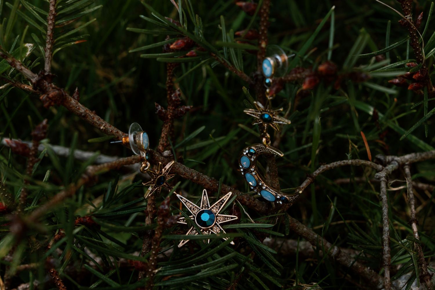 Celestial star and moon pendants with turquoise stones hang delicately among dark green pine tree branches.