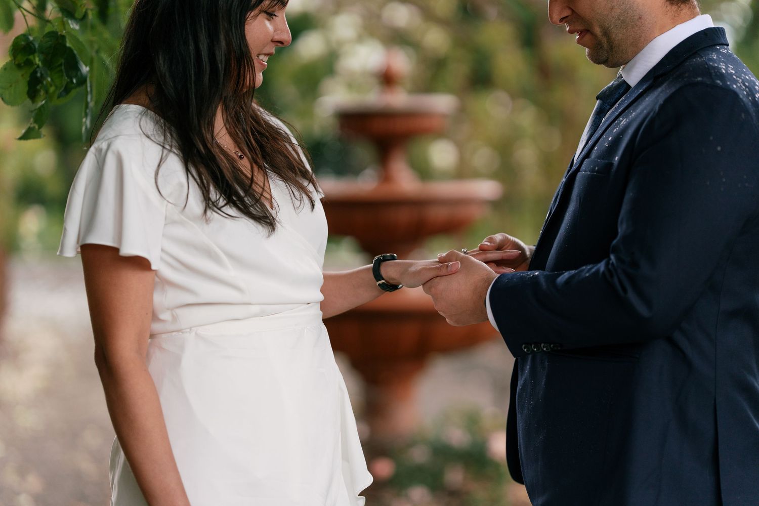 Groom placing wedding ring on brides finger during intimate garden elopement ceremony.