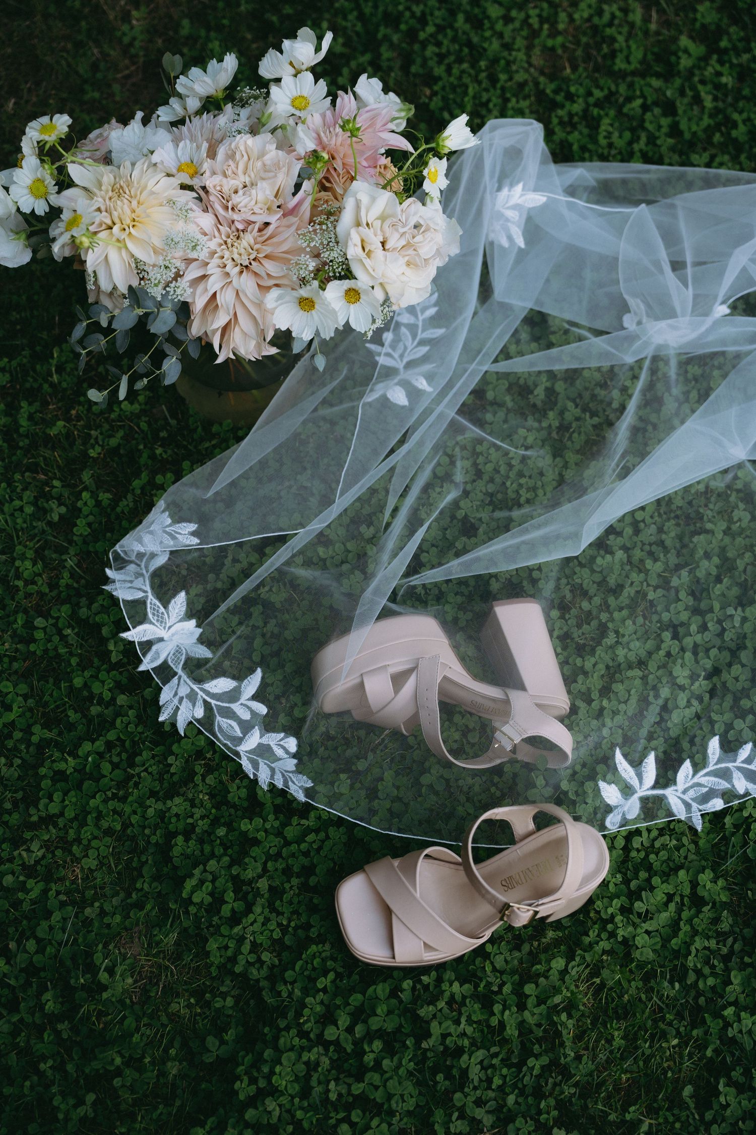 Bridal veil, blush heels, and floral bouquet with dahlias arranged on green moss.