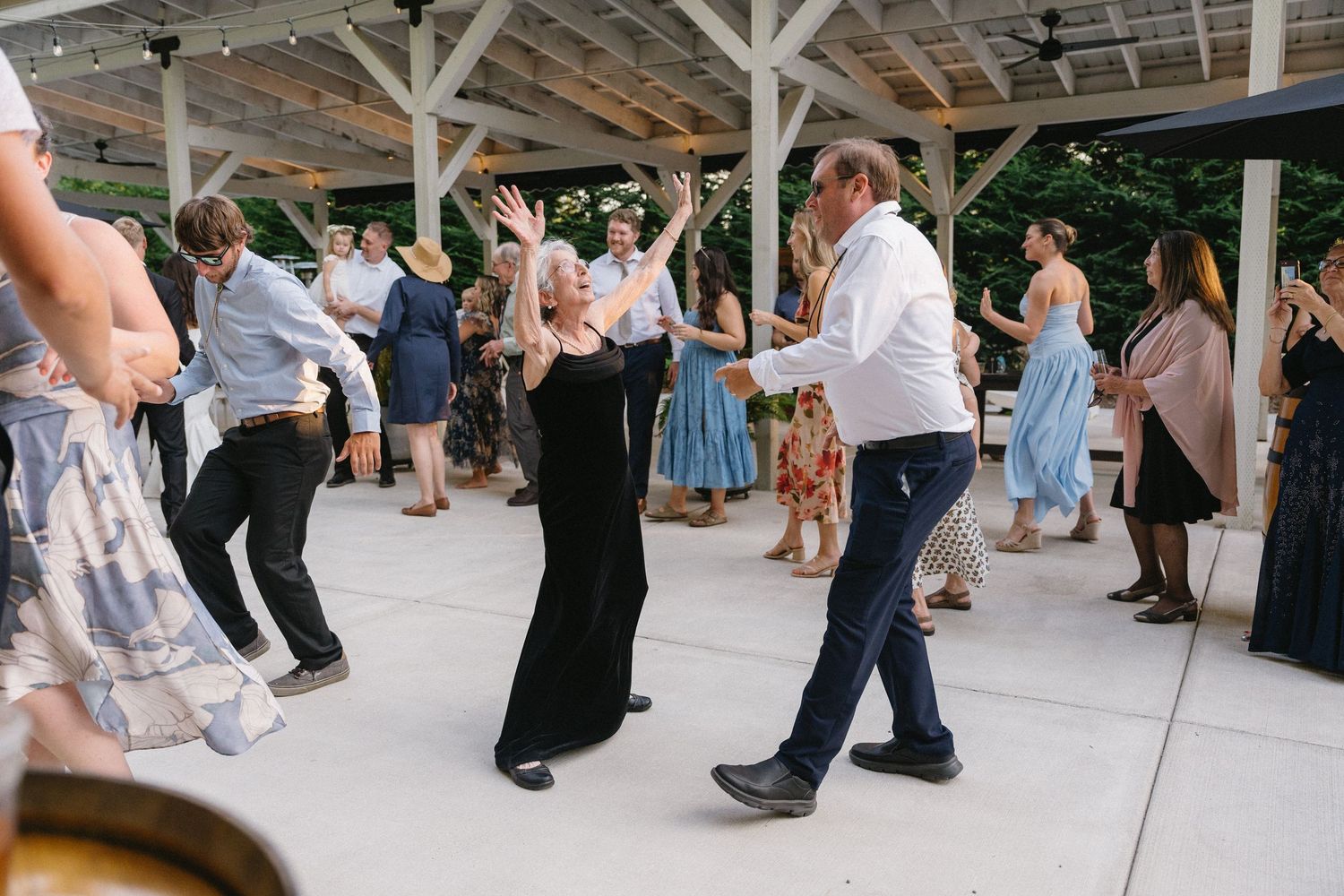 Energetic wedding guests dancing together under pavilion at lively outdoor reception celebration.