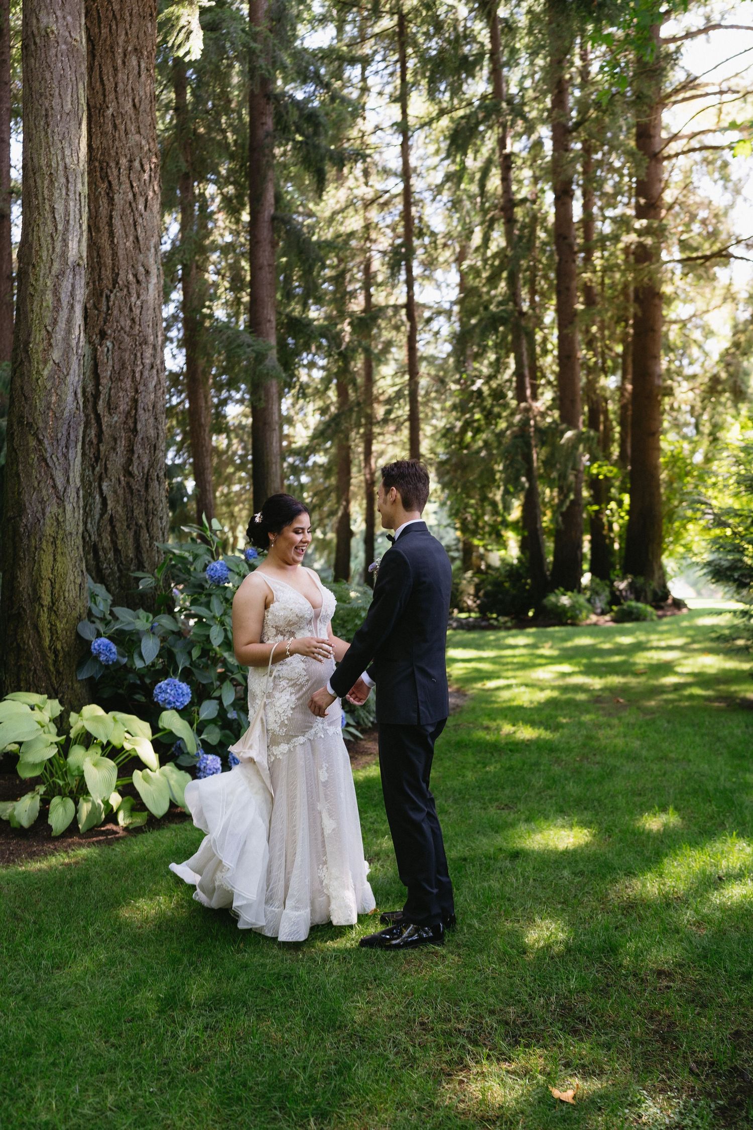 Bride and groom holding hands facing each other in a lush garden with blue hydrangeas.