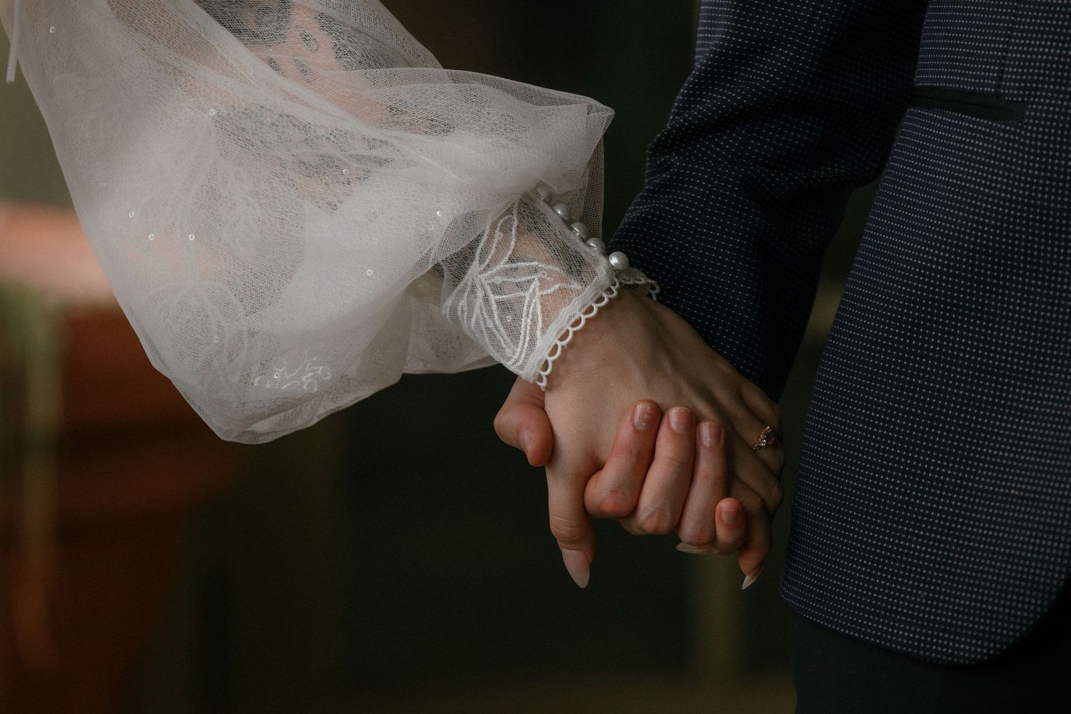 Close-up of bride and groom holding hands, bride wearing a pearl bracelet with veil detail.