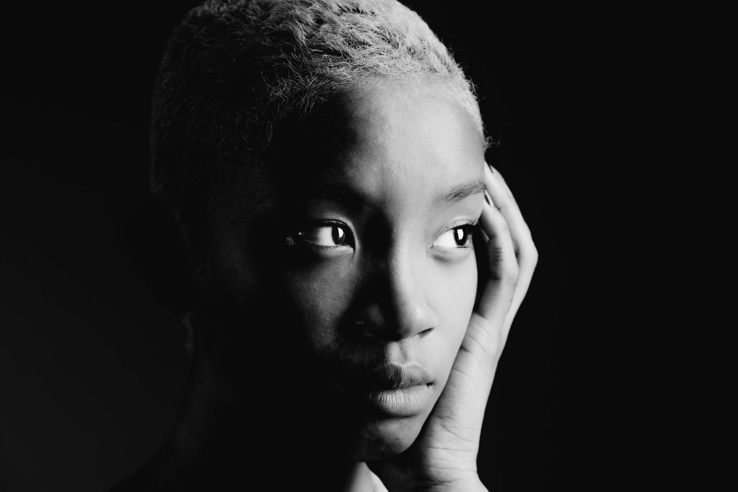 Striking black and white close-up portrait of a person with short hair resting hand against their face.