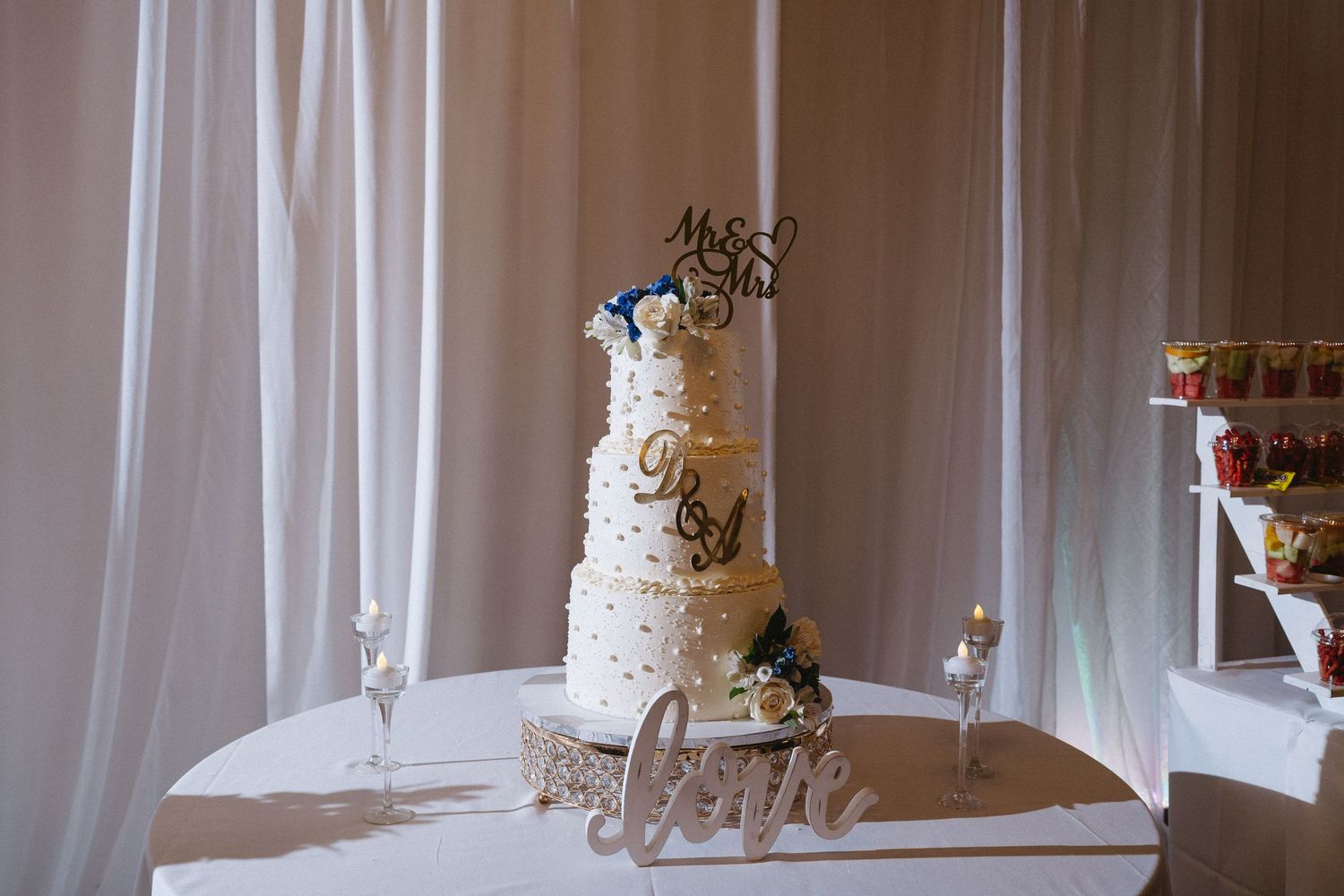 Elegant four-tier white wedding cake with Mr & Mrs topper on decorated table.