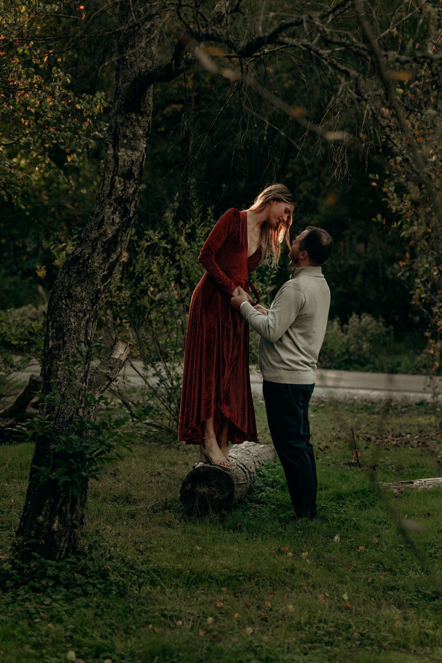 Woman in red velvet dress standing on a log holding hands with man in autumn forest.