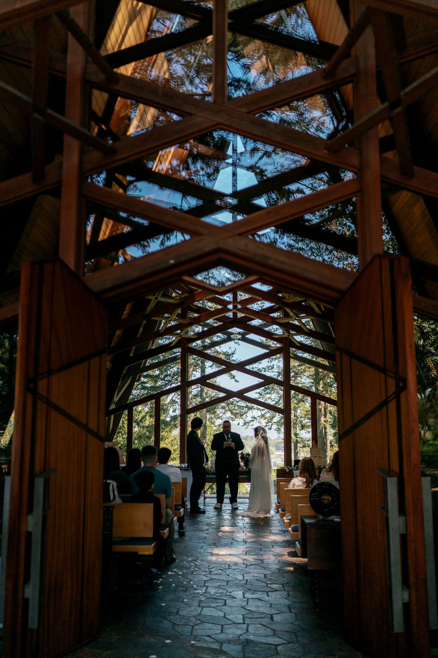 Wedding ceremony inside a stunning glass and wood chapel with guests seated in pews.