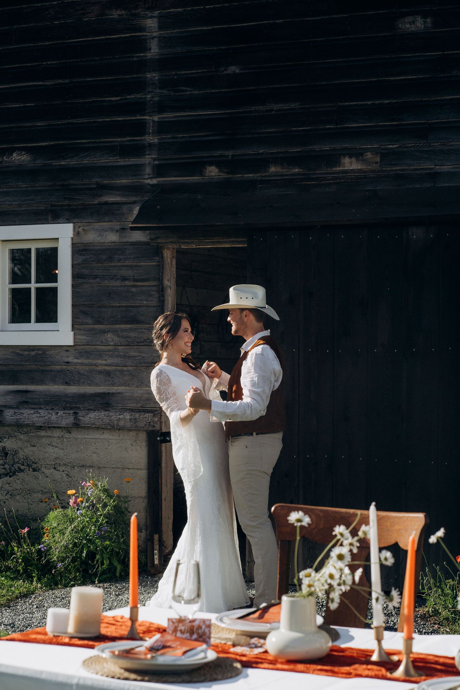 Bride and groom sharing first dance beside decorated outdoor wedding table at rustic barn.