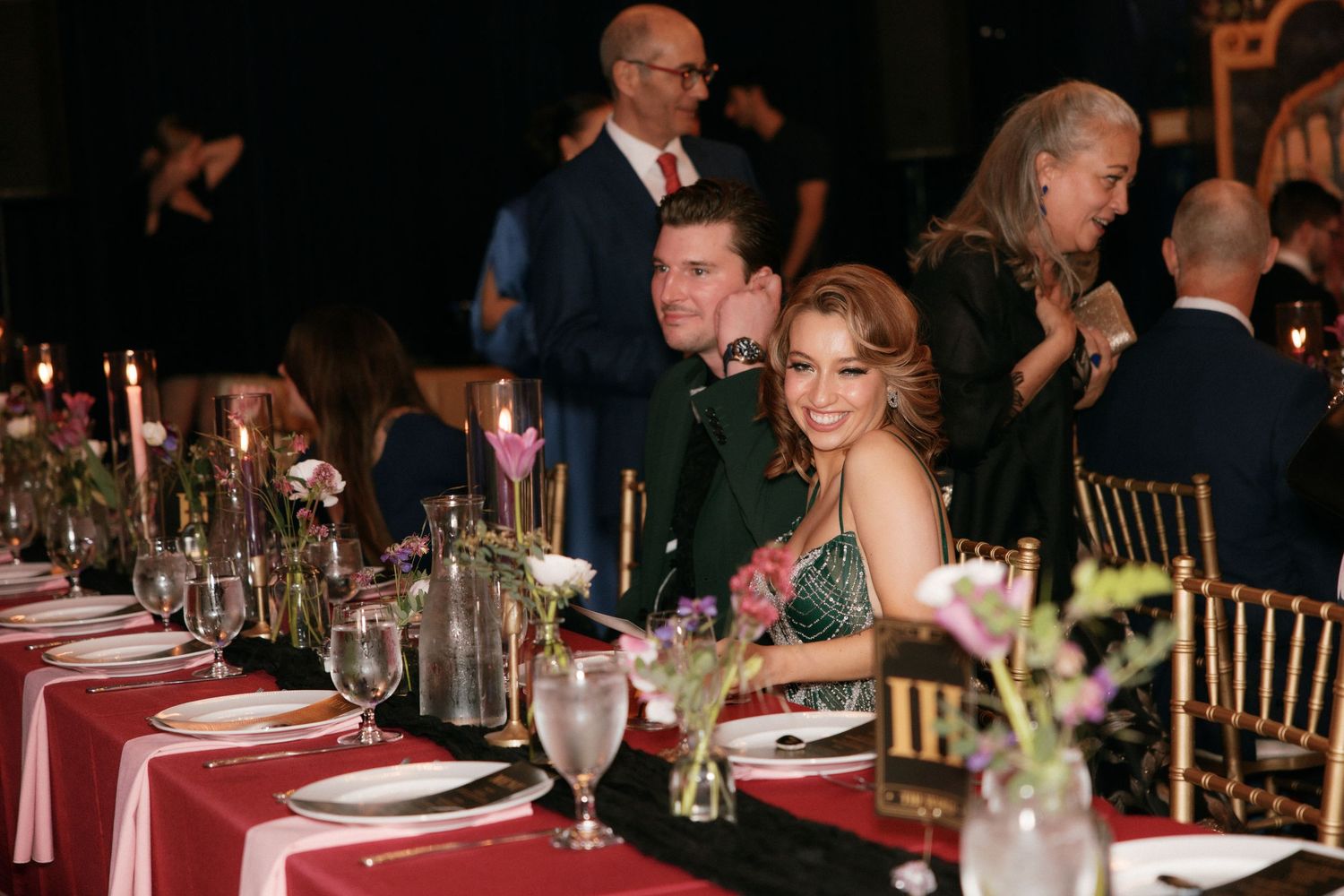 Smiling couple poses at elegantly set wedding reception dinner table with floral centerpieces.