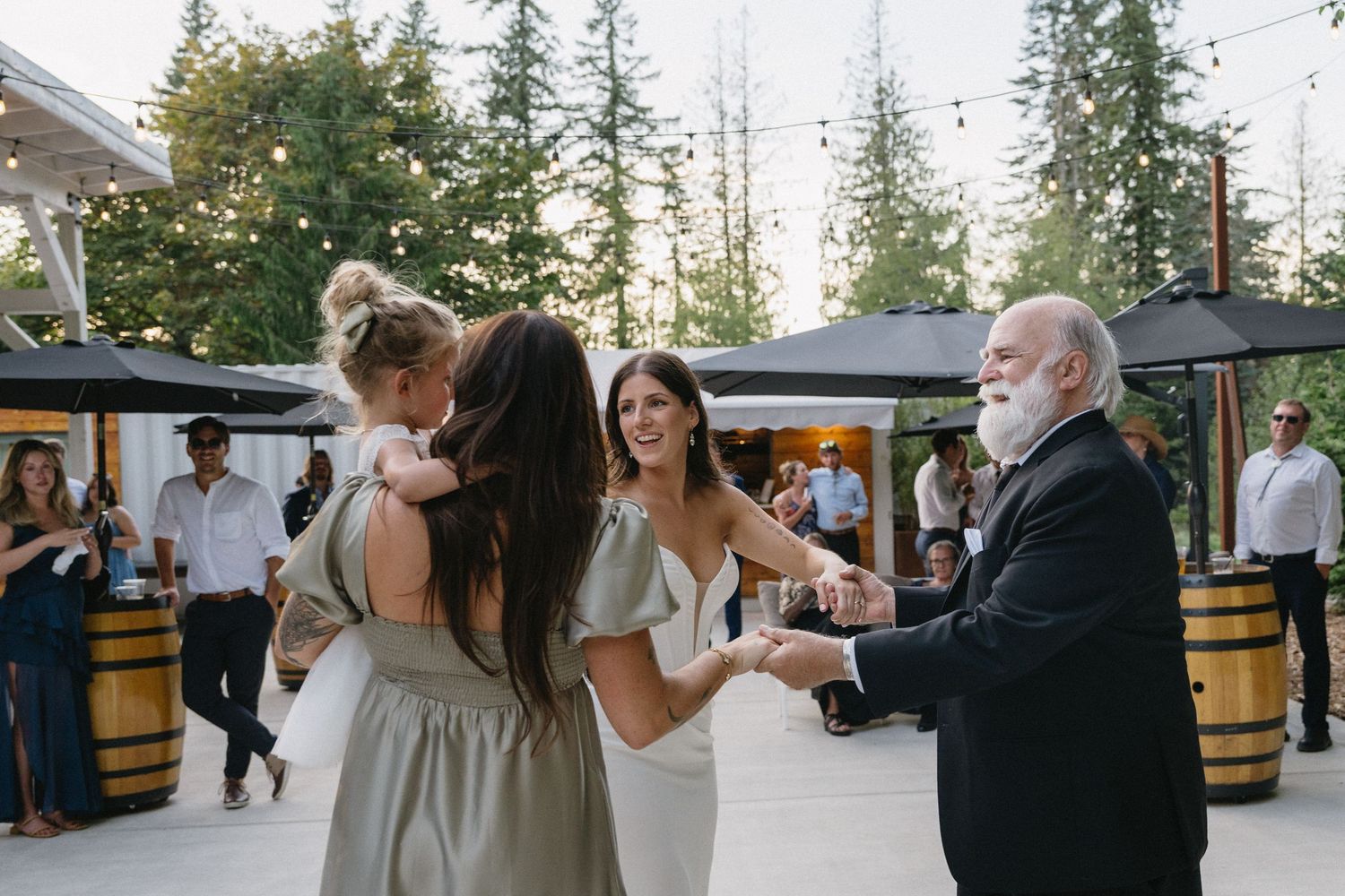Wedding guests dancing and celebrating on outdoor patio with string lights and barrel decorations.