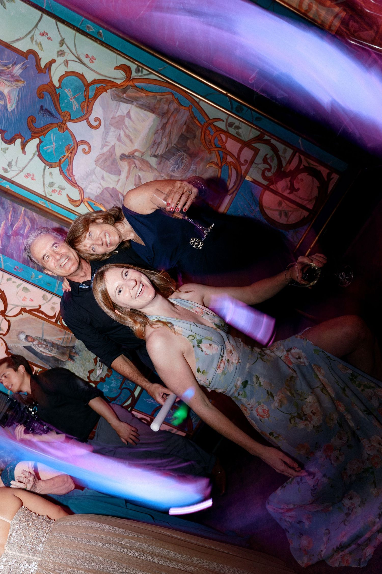 Smiling wedding guests posing together in an ornately decorated venue with vibrant murals.