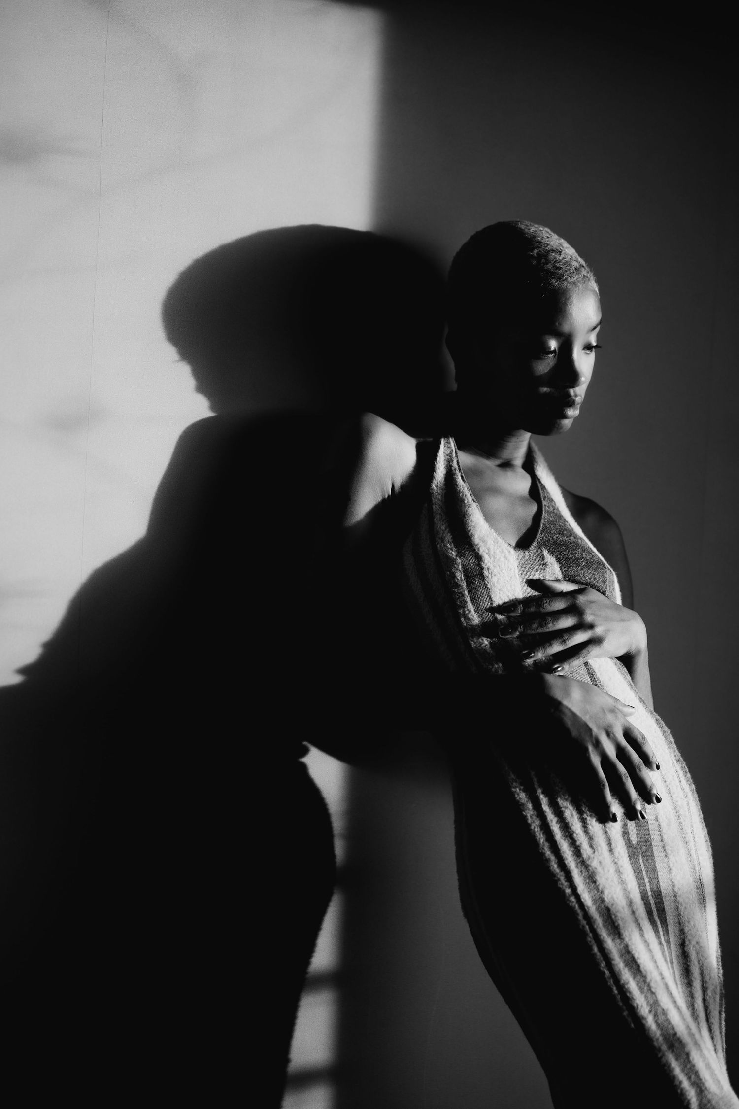 Artistic black and white portrait of a woman in a striped dress with dramatic shadow cast on the wall beside her.