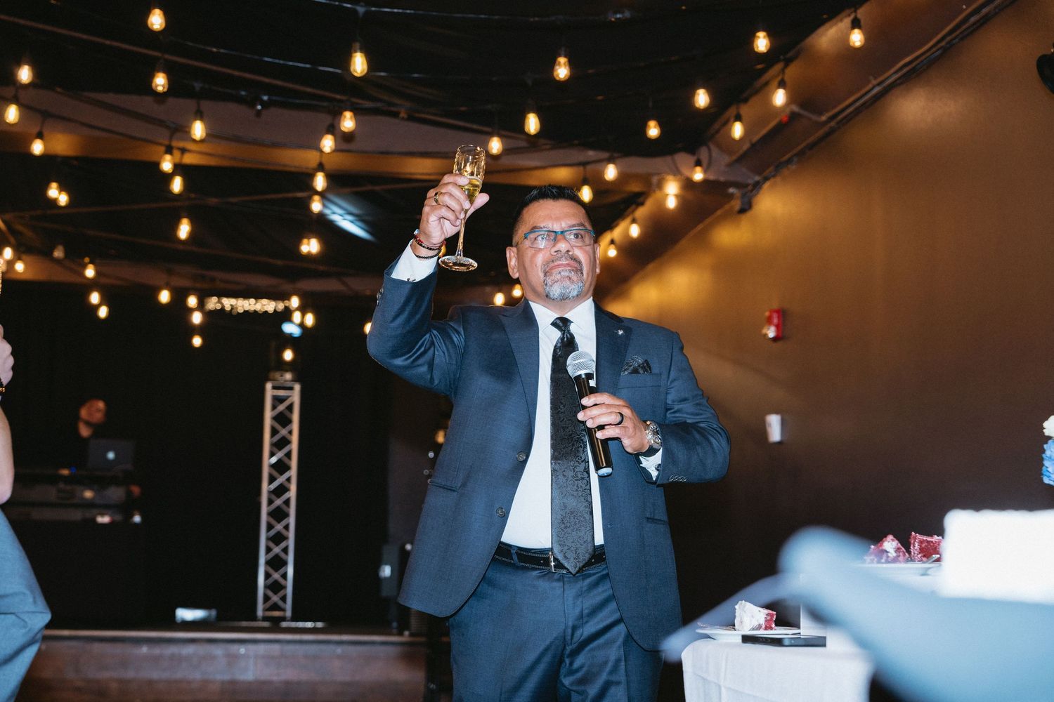 Man in suit raising champagne glass while giving toast at wedding reception.