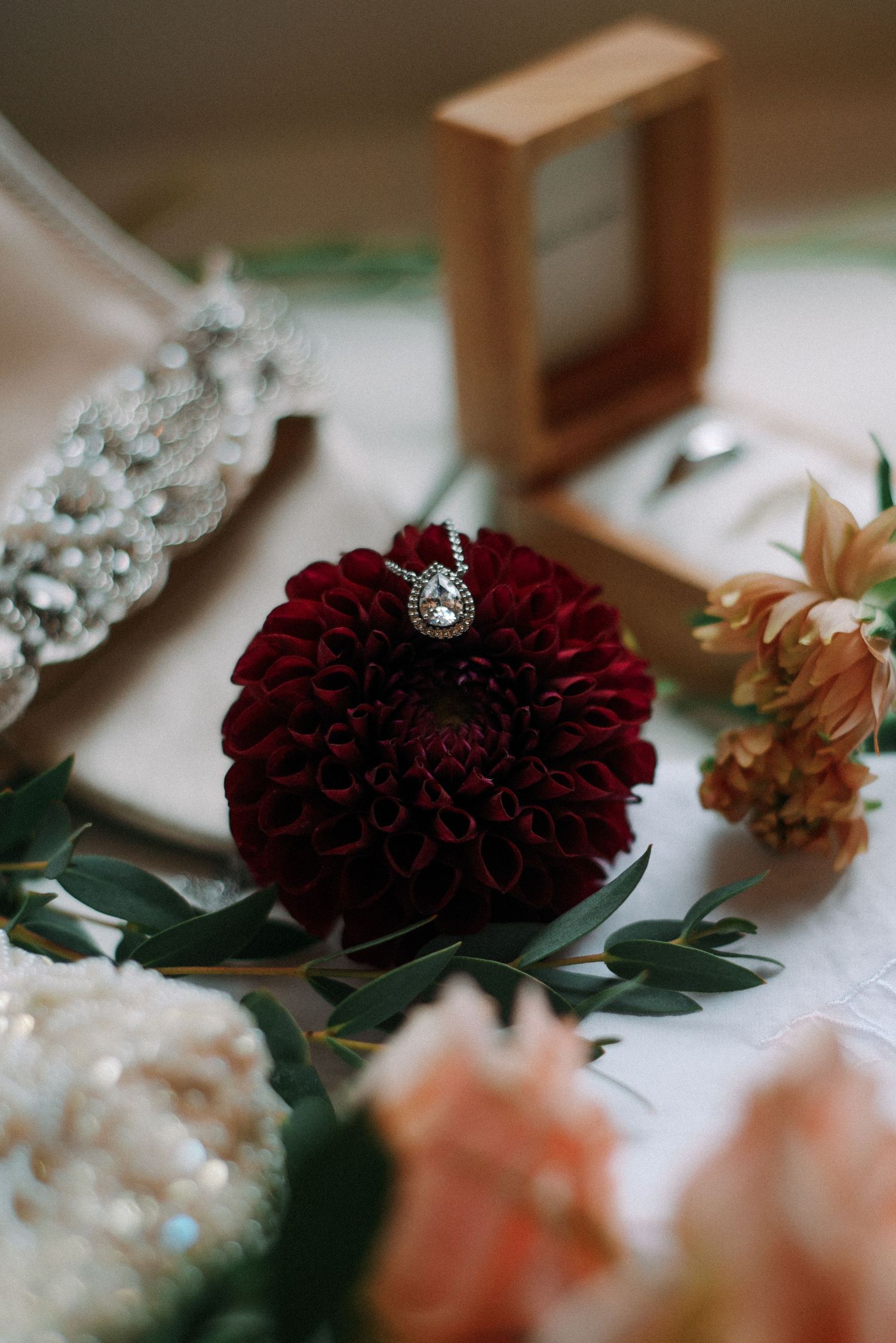Diamond engagement ring resting on deep red dahlia flower surrounded by wedding jewelry and floral decor.