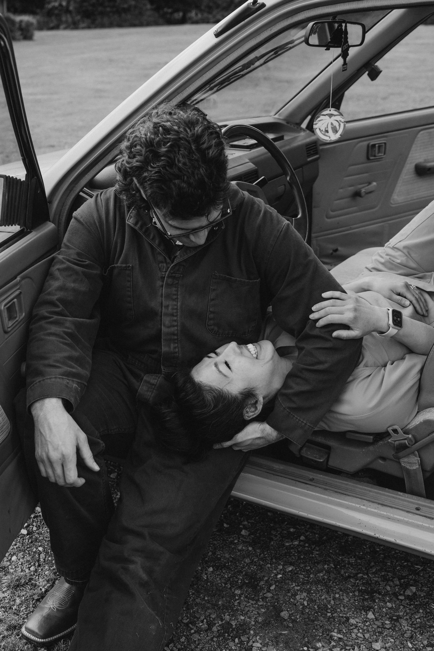 Black and white photo of a couple sharing an intimate moment inside a vintage car.