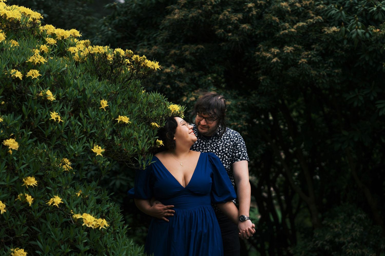 Romantic couple holding hands and gazing at each other beside yellow blooming flowers in a garden.