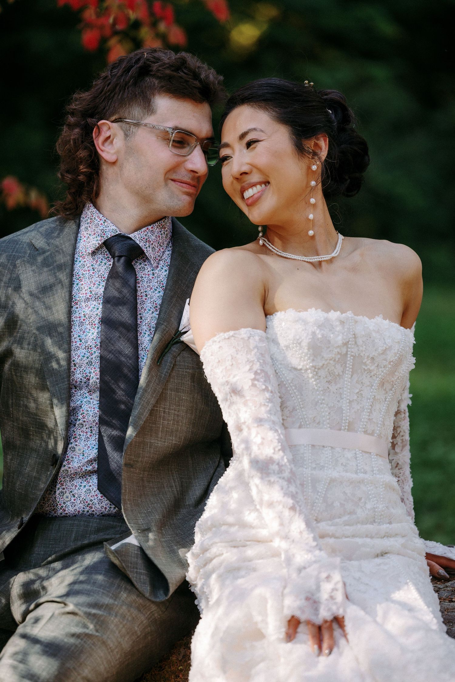 Interracial couple shares a joyful moment in wedding attire, groom in gray suit, bride in strapless lace gown.