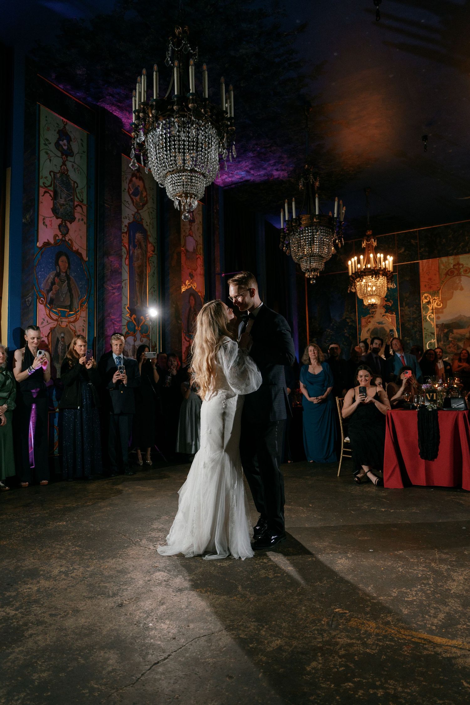 Bride and groom share first dance under crystal chandeliers at wedding reception.