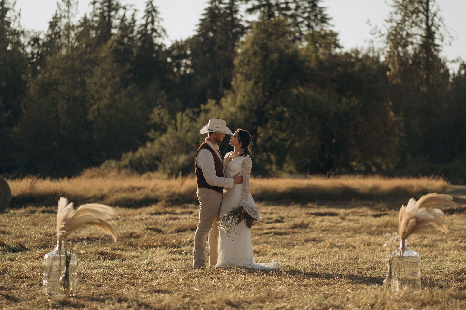 Bride and groom embrace in a golden sunlit open field with pampas grass decor at a rustic outdoor wedding.