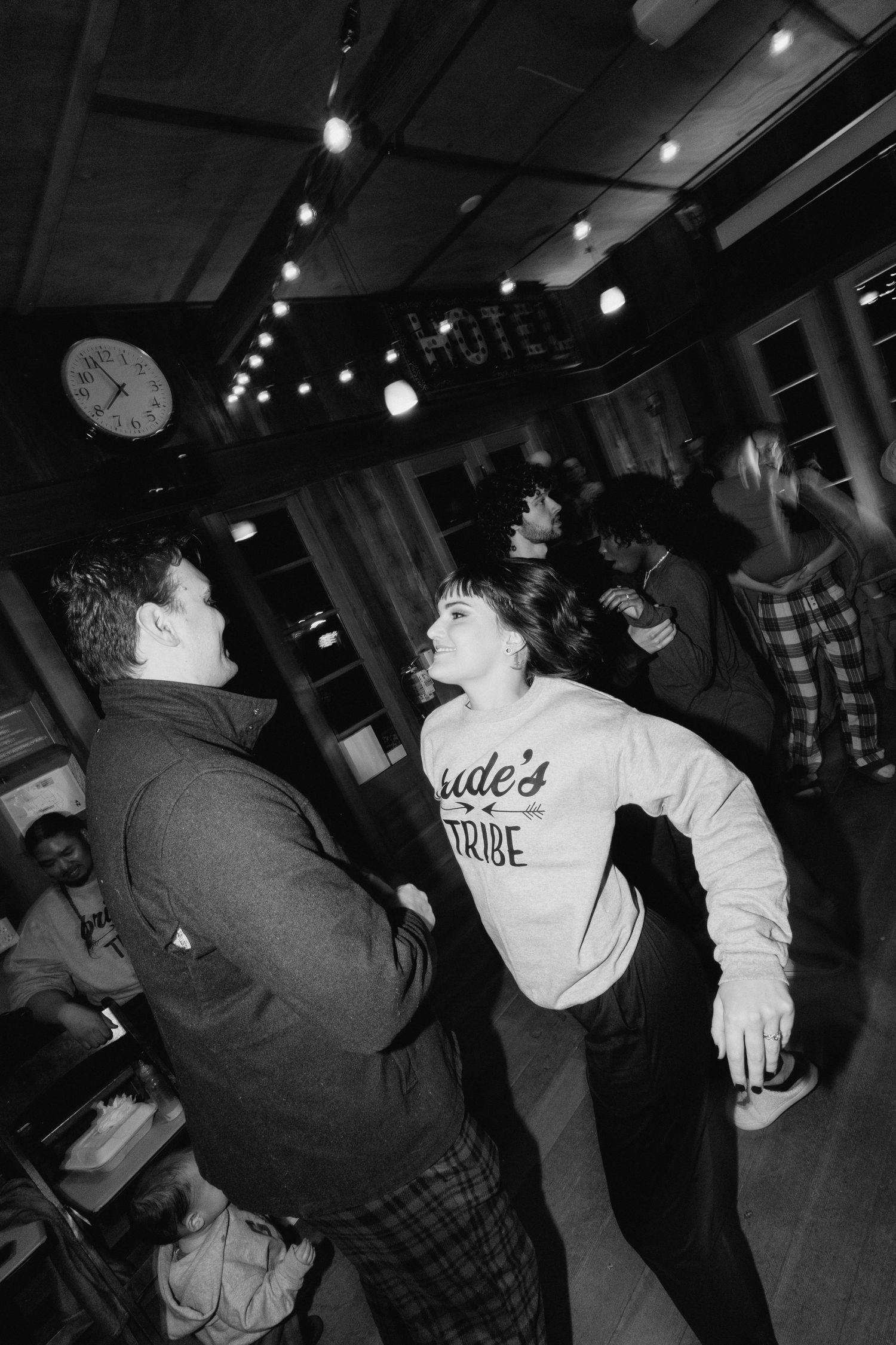 Guests dancing at an informal wedding party wearing Bride's Tribe sweatshirts under string lights.