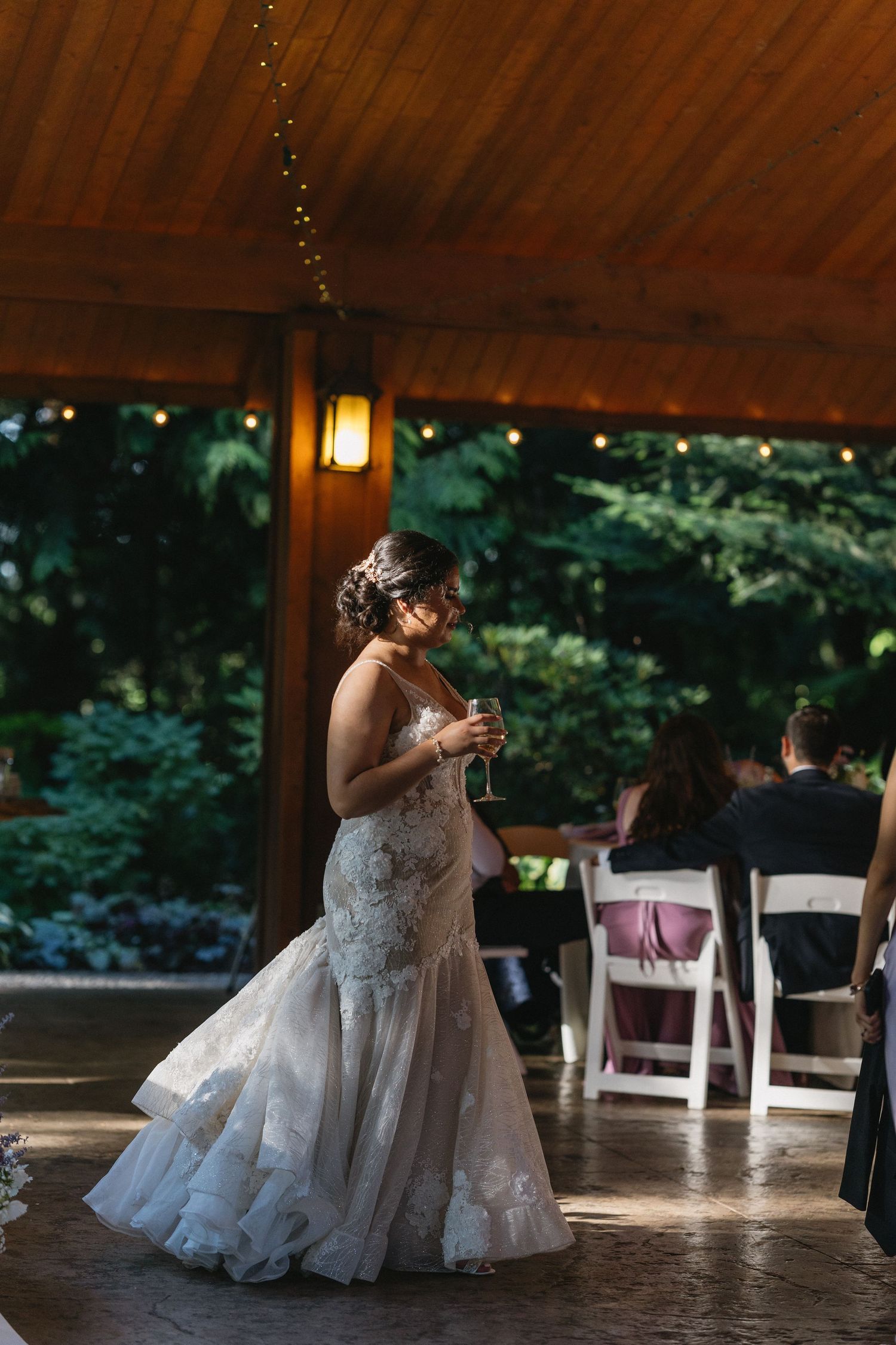 Elegant bride in lace mermaid gown holds a glass while standing alone on the dance floor.
