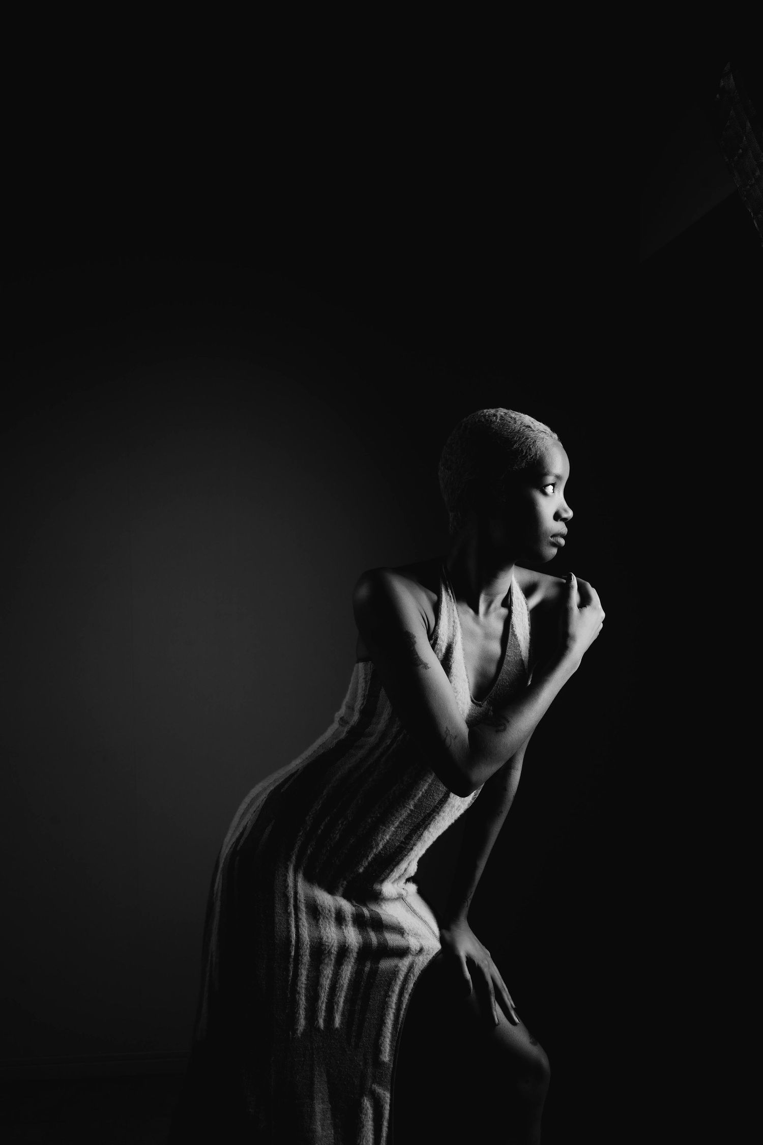 Elegant black and white portrait of a woman in a striped dress posing gracefully against a dark background.
