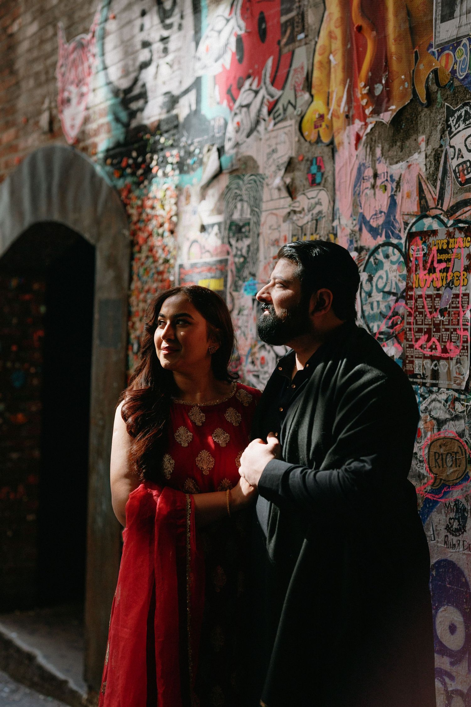 Couple in traditional Indian attire sharing a tender moment against a colorful graffiti-covered wall.