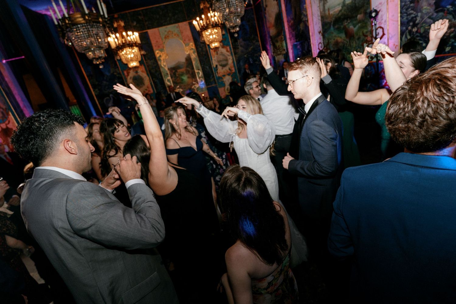 Wedding guests dancing energetically on crowded dance floor at reception.