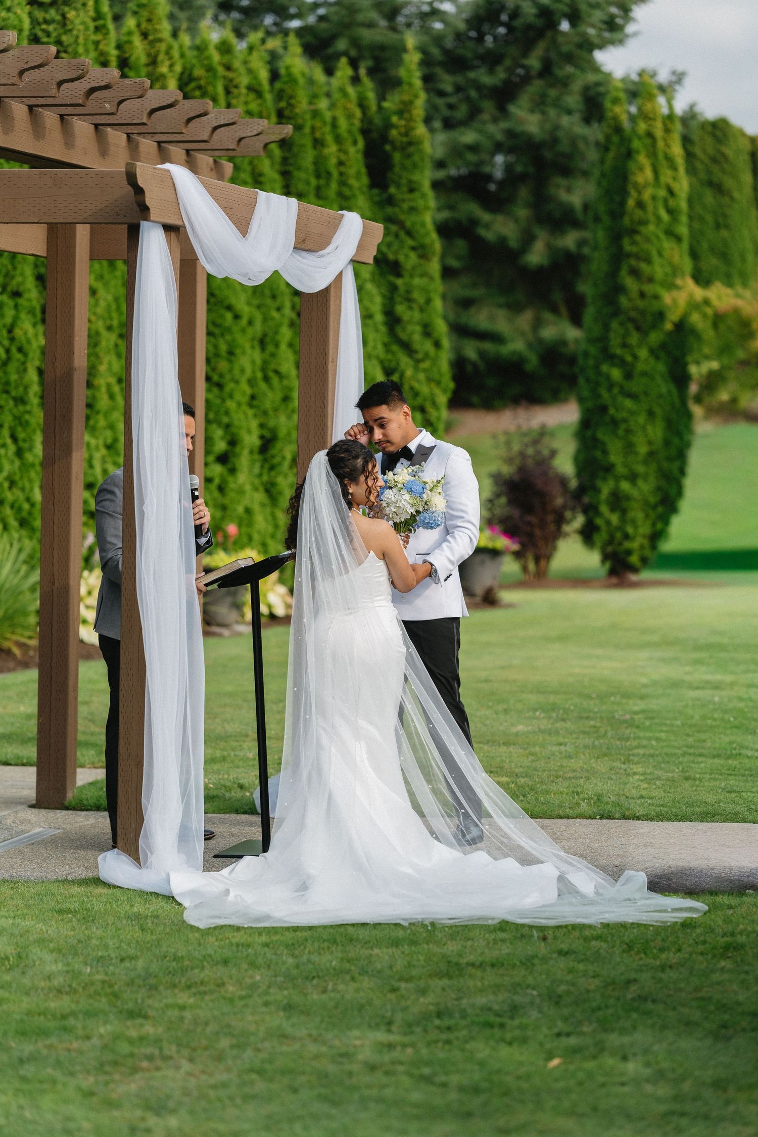 Bride and groom share first kiss under elegant draped pergola altar at outdoor garden wedding ceremony.