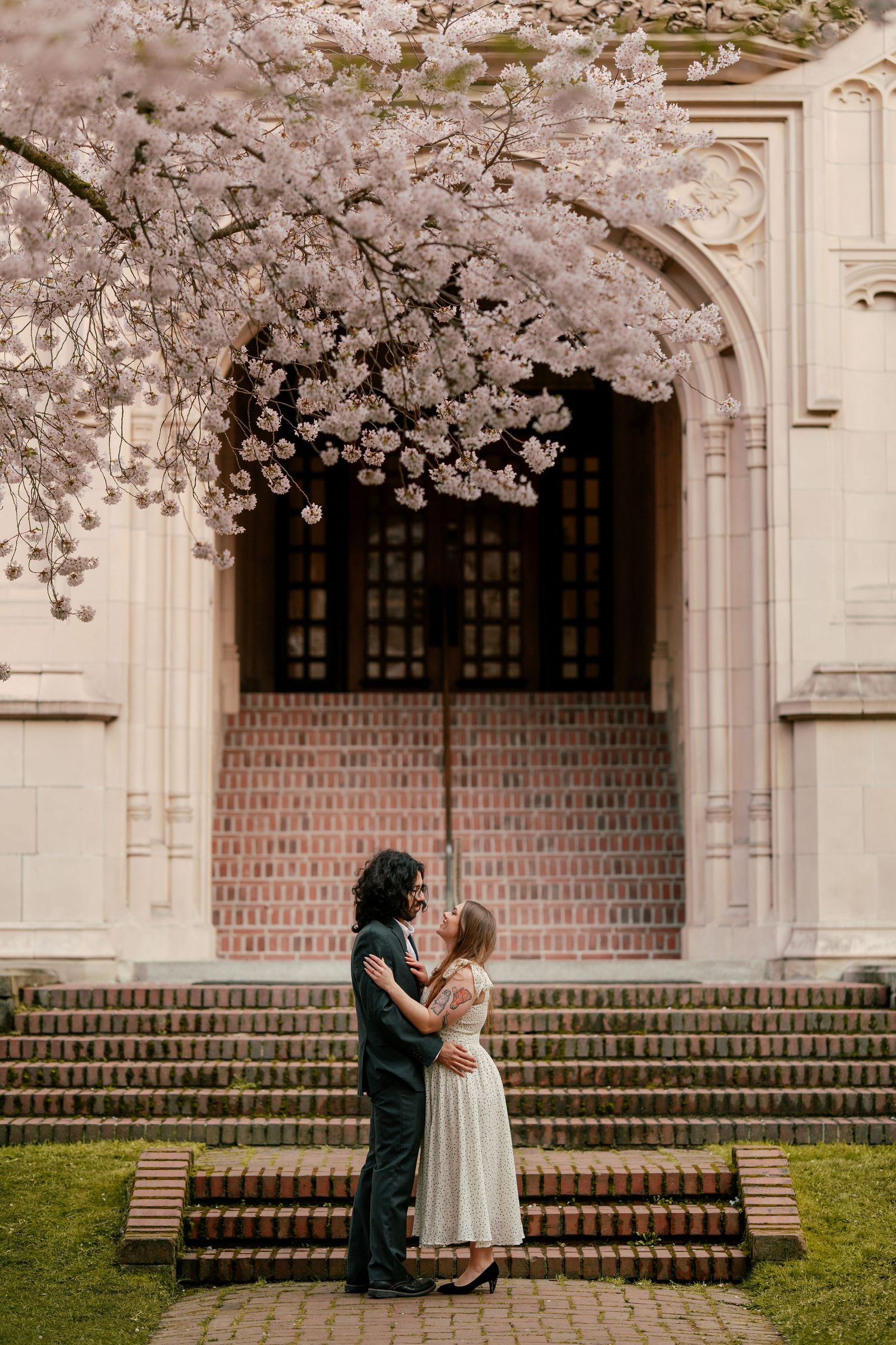 Couple sharing a kiss under blooming cherry blossom branches in front of an ornate arched doorway.