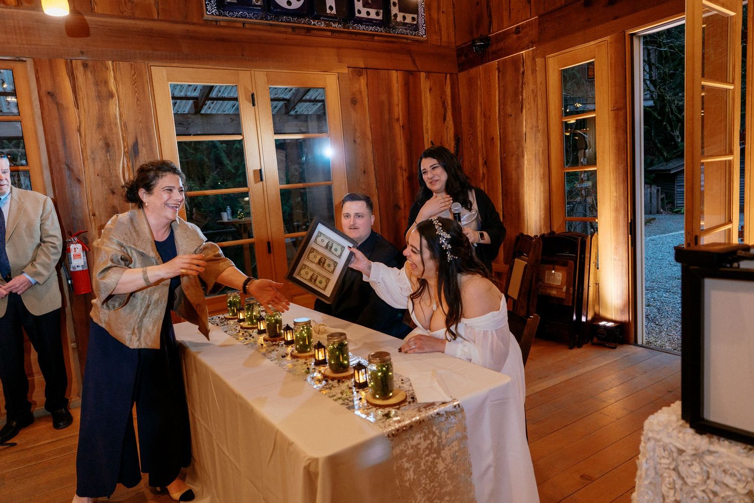 Guest presents framed gift to bride at decorated wedding reception head table with candles.
