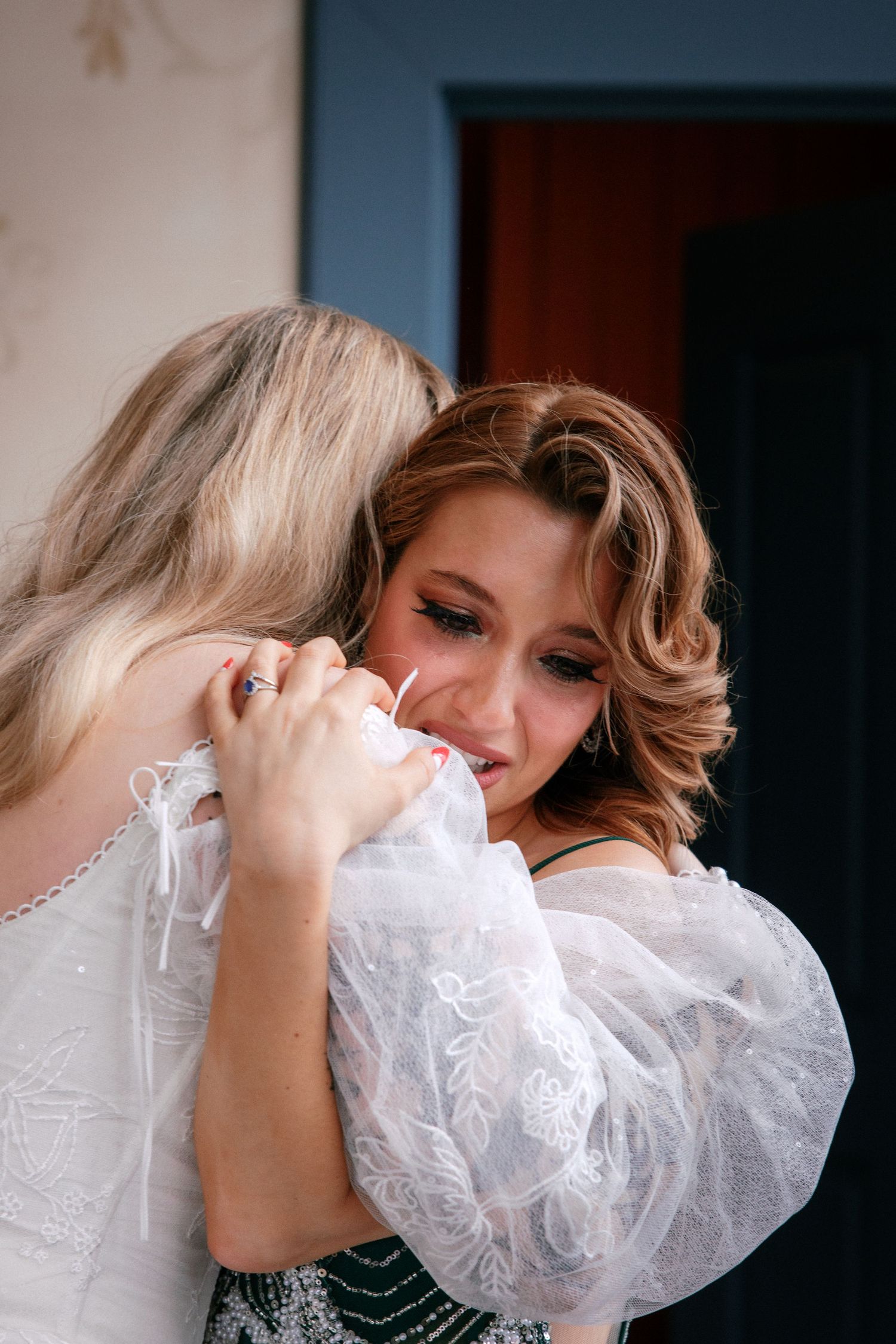 Two women sharing an emotional embrace at a wedding, one wearing a white bridal gown.