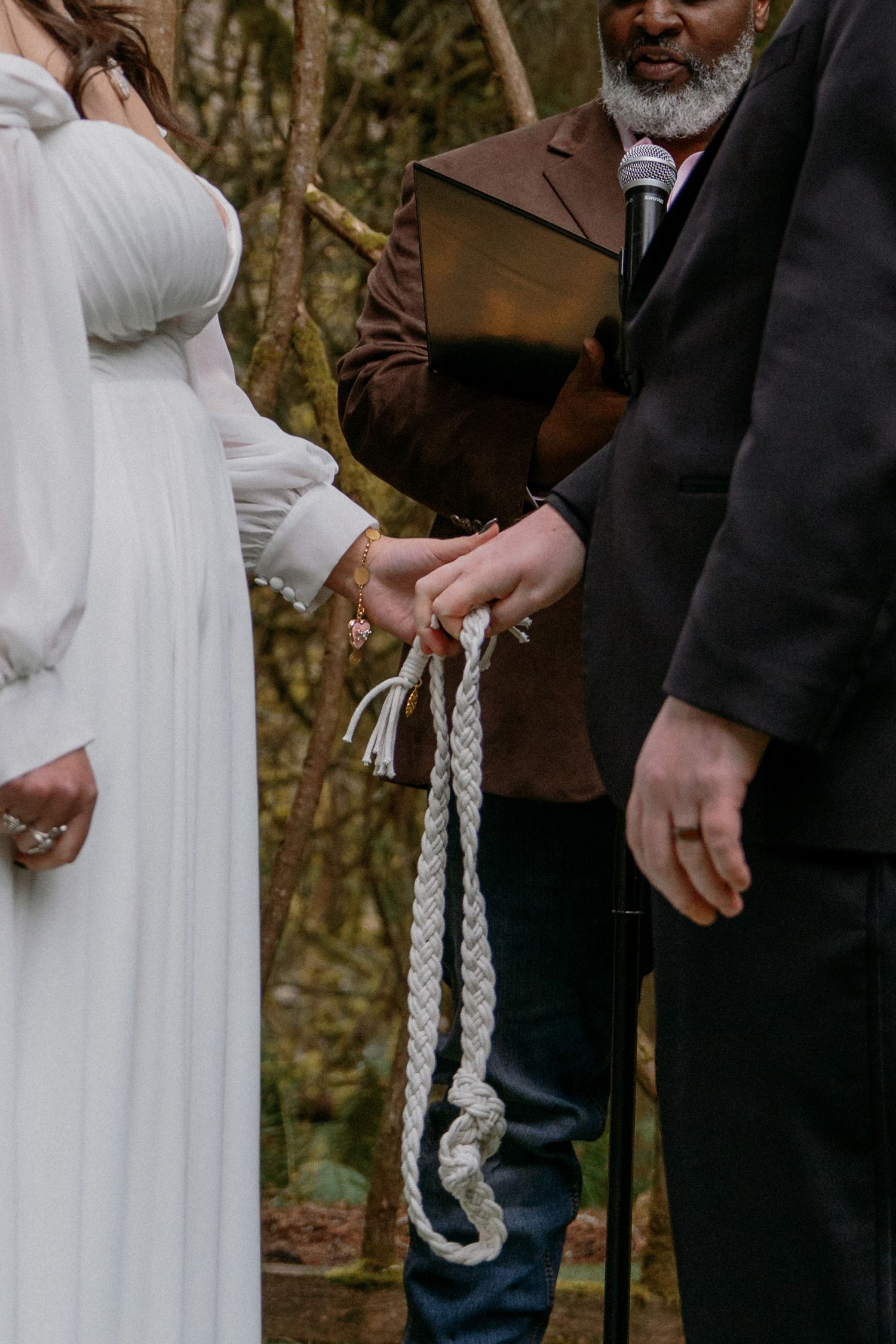 Close-up of bride and groom hands tied with braided rope during hand-fasting wedding ceremony.