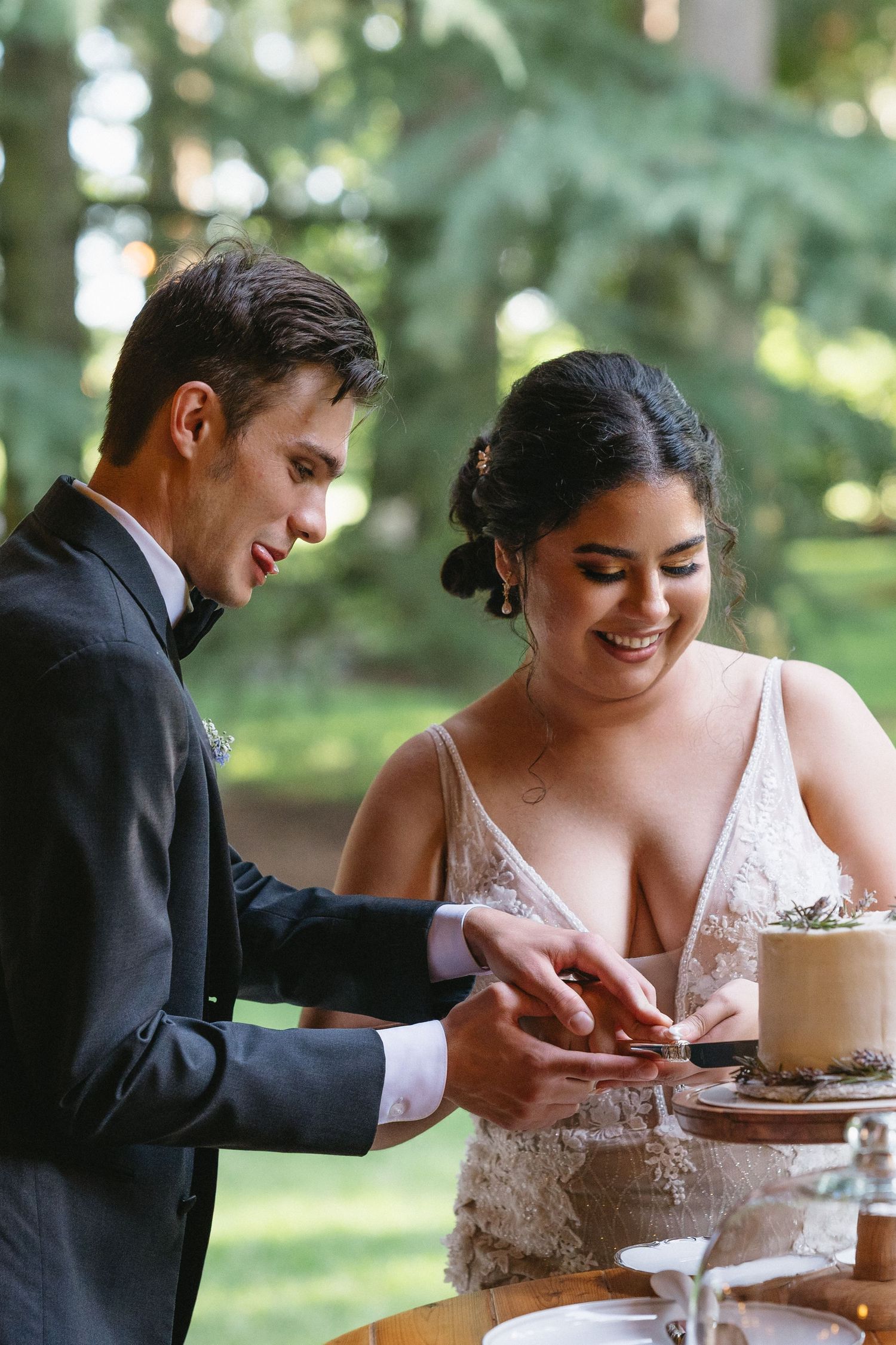 Smiling bride and groom cutting wedding cake together at elegant outdoor garden reception.