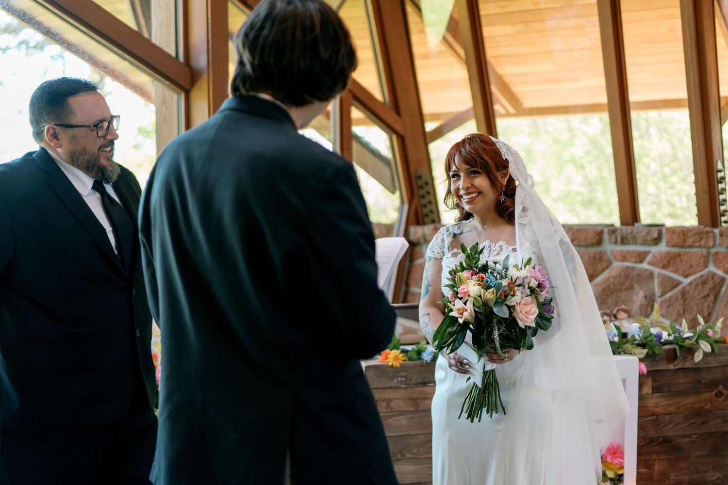 Bride smiling holding a bouquet during wedding ceremony with officiant and groom.