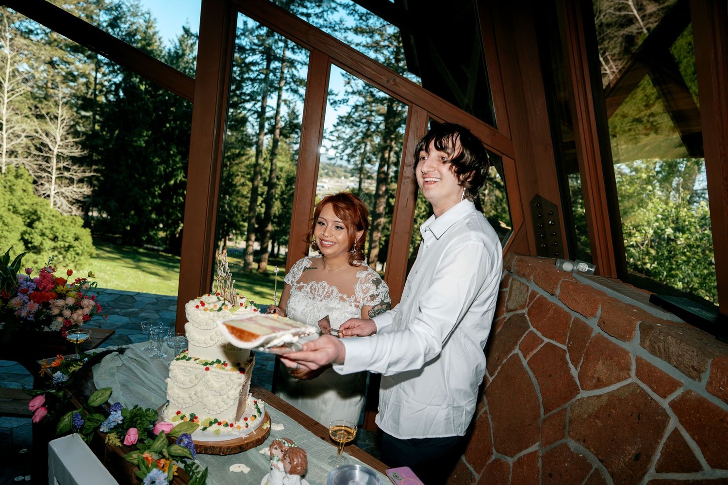 Bride and groom smiling while cutting their decorated white tiered wedding cake.