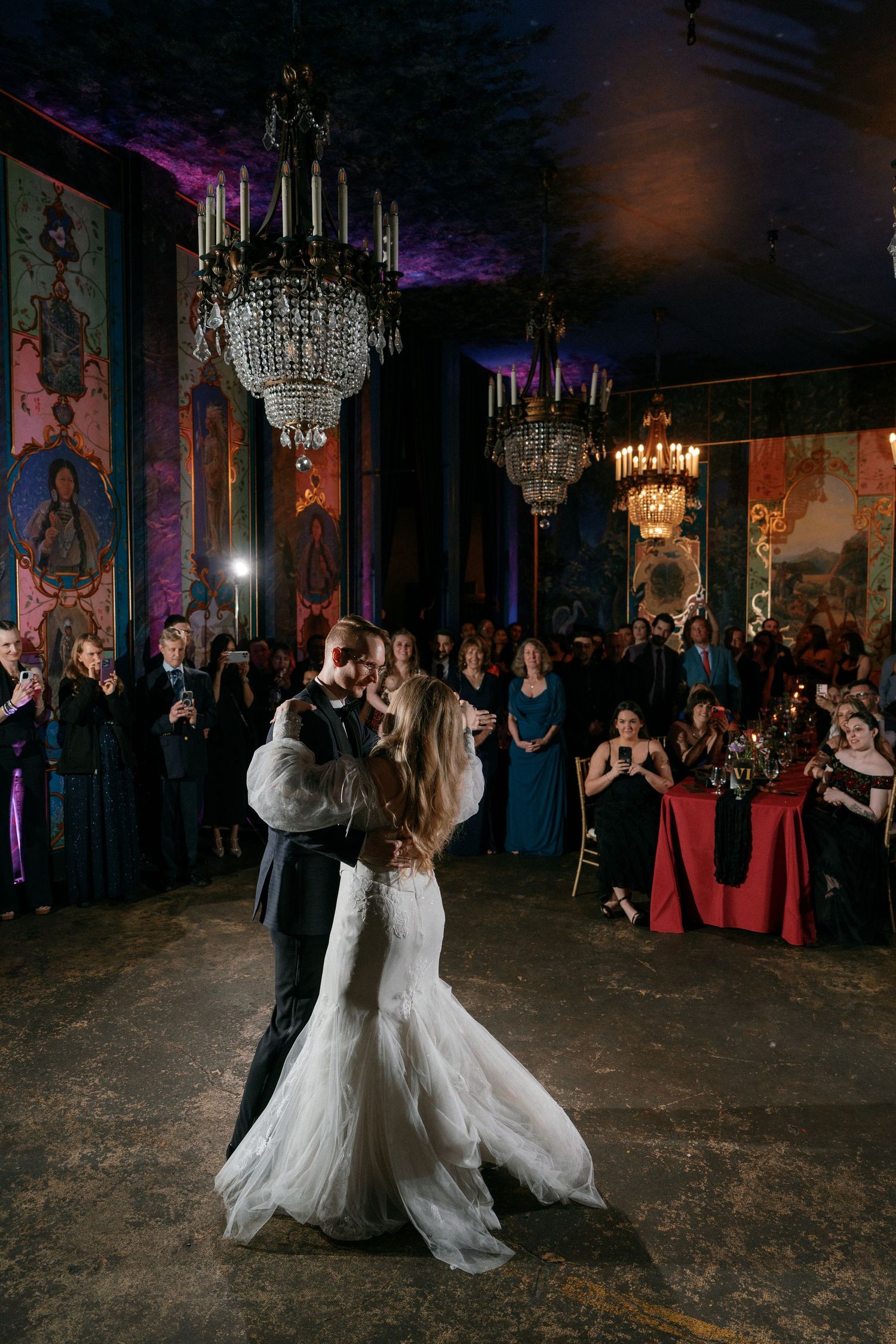 Bride and groom share romantic first dance surrounded by wedding guests.