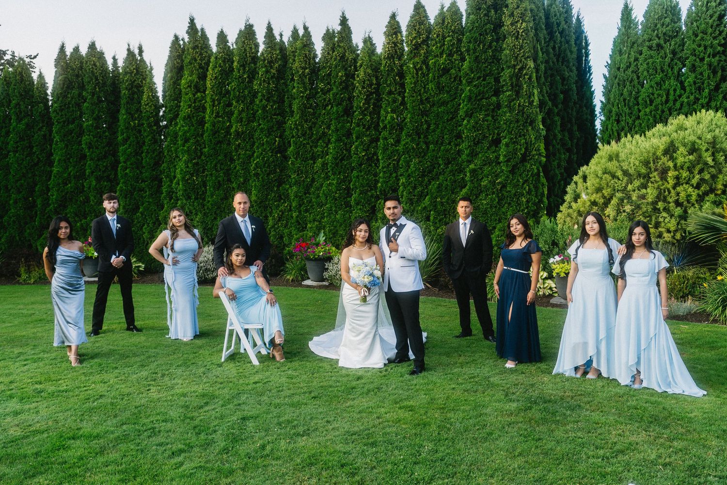 Wedding party poses on green lawn with bride, groom, and attendants in blue.