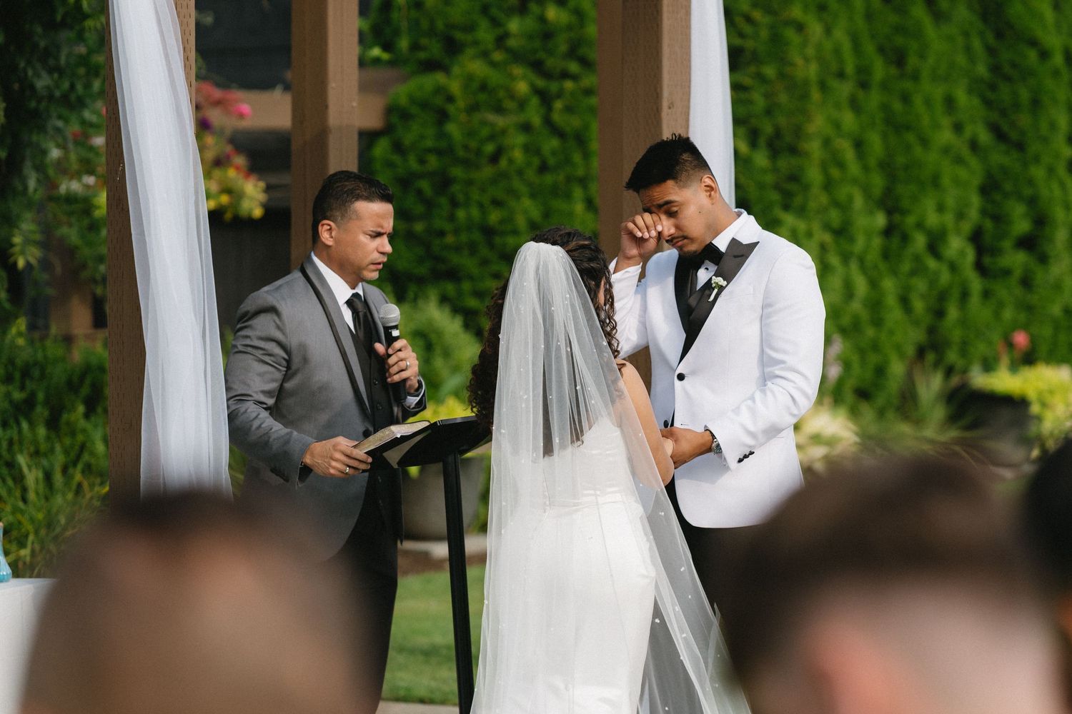 Emotional bride and groom share a tender moment as the officiant reads during their outdoor wedding ceremony.
