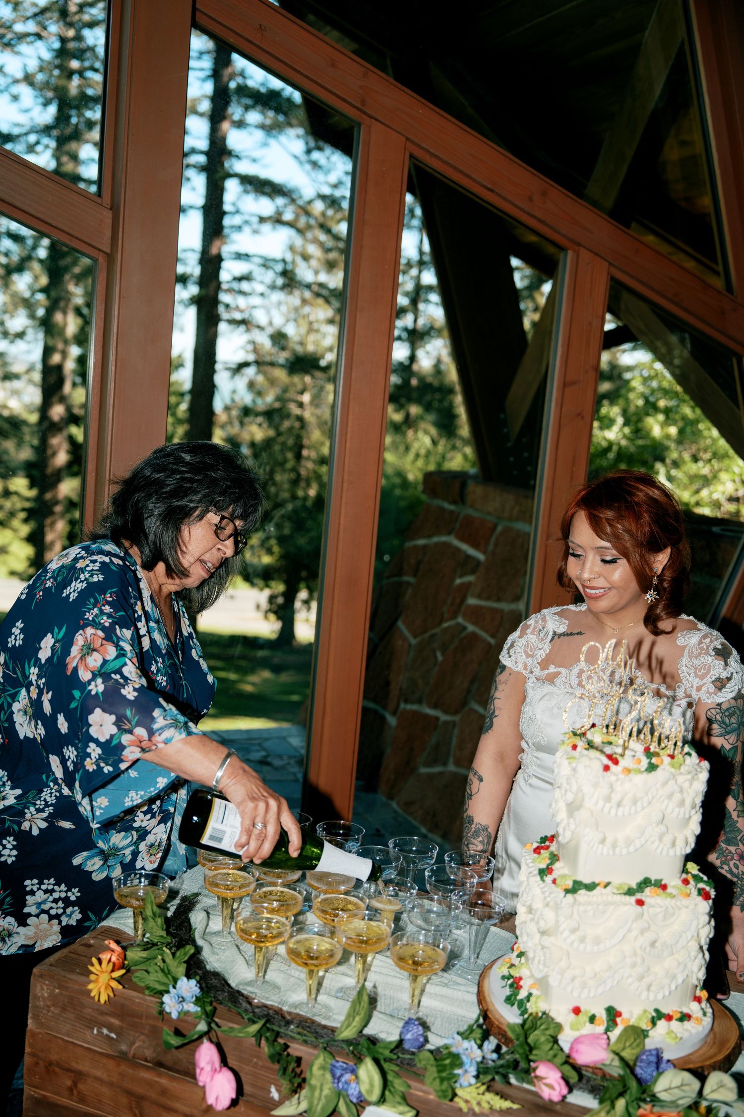 Woman pouring champagne at wedding reception table beside tiered white wedding cake.