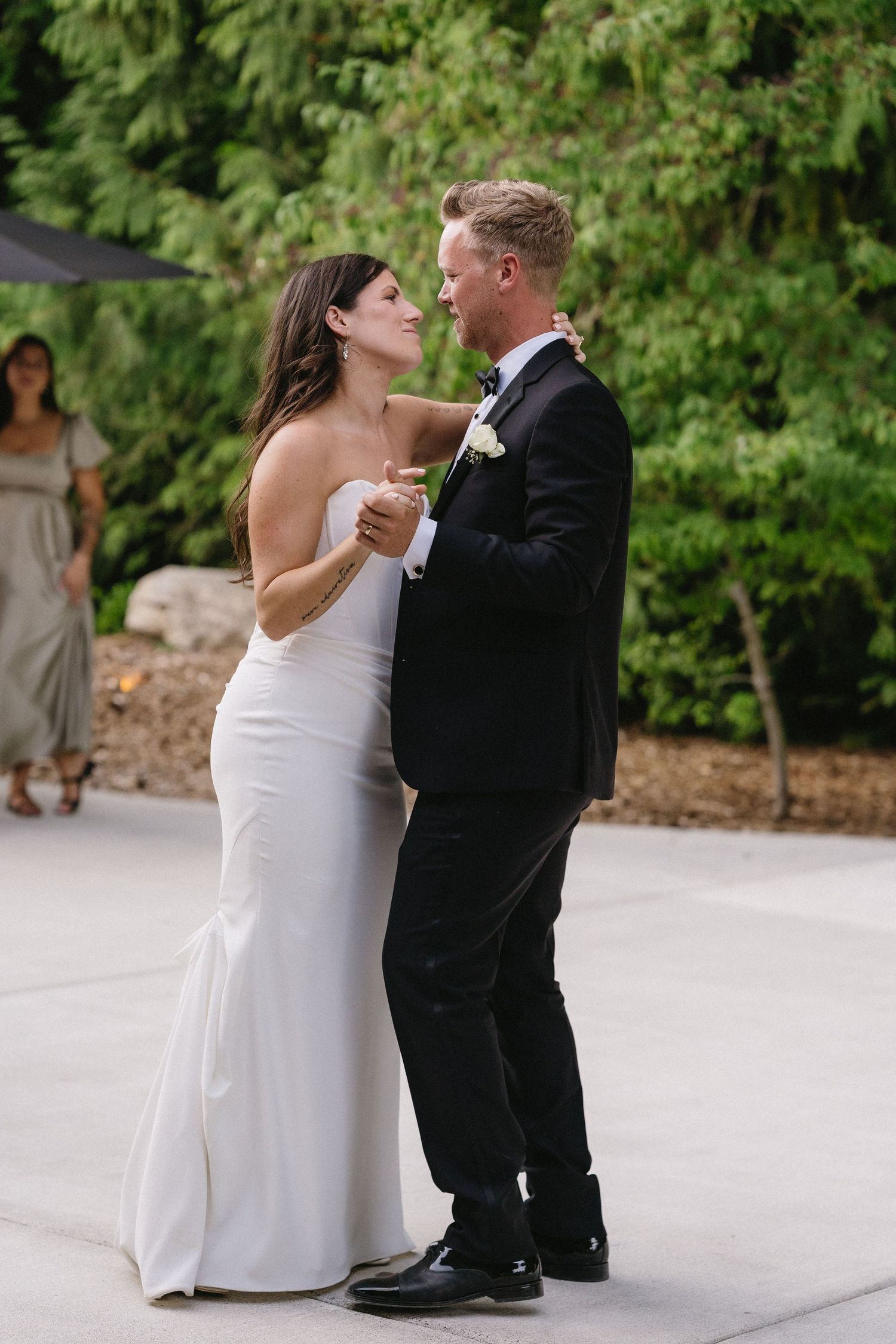 Bride in white gown and groom in black tuxedo sharing first dance at outdoor wedding reception.