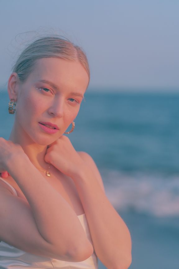 Close-up portrait of blonde woman with hoop earrings at ocean beach during golden hour.