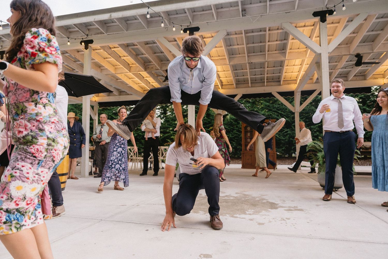 Wedding guest performing impressive leap over crouching person on dance floor at reception.